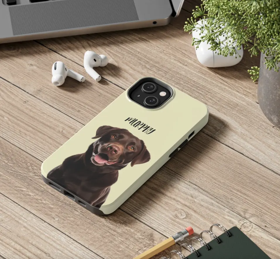 Custom phone case with 'Murphy' the chocolate Labrador's portrait on a wooden desk.